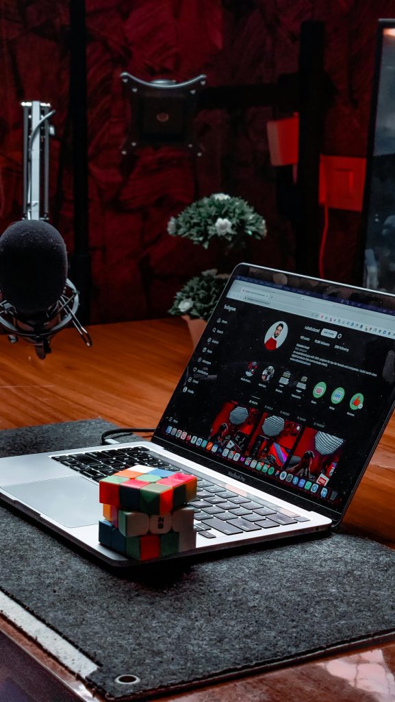 Modern workspace featuring a laptop, Rubik's Cube, and podcast microphone in a studio setting.